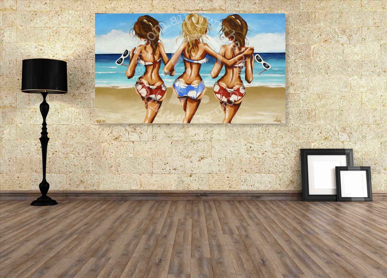 Painting of three women in swimsuits on a beach wall in a room with a lamp and frames.