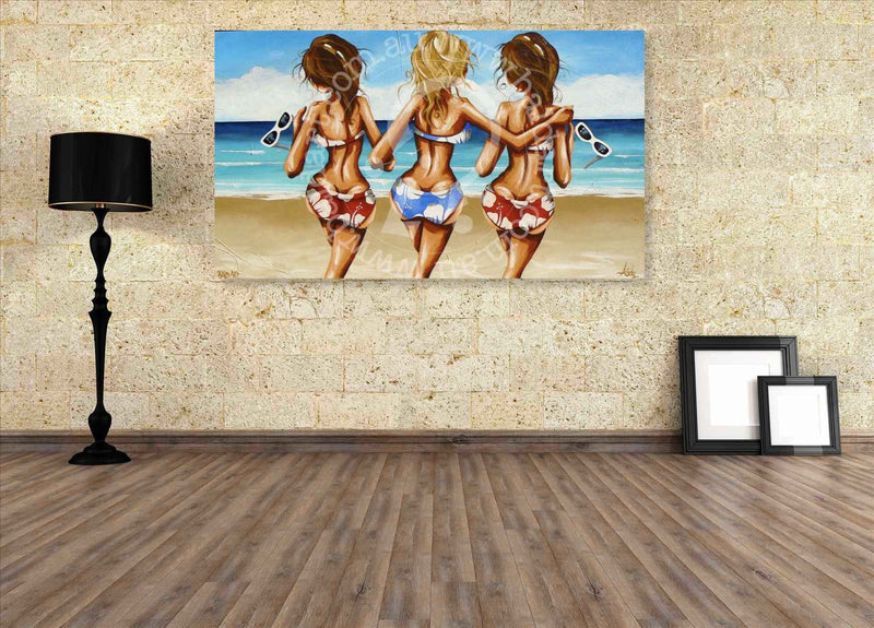 Painting of three women in swimsuits on a beach wall in a room with a lamp and frames.