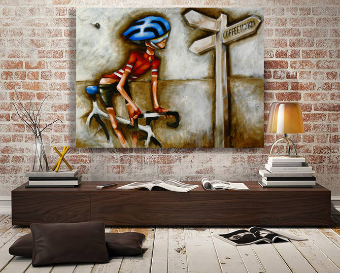 Contemporary cycling wall art by Bald Art displayed in a loft-style room, featuring a cyclist in red near a signpost reading ‘Coffee 12 km’ from The Cycle Series.