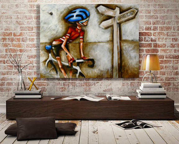 Contemporary cycling wall art by Bald Art displayed in a loft-style room, featuring a cyclist in red near a signpost reading ‘Coffee 12 km’ from The Cycle Series.