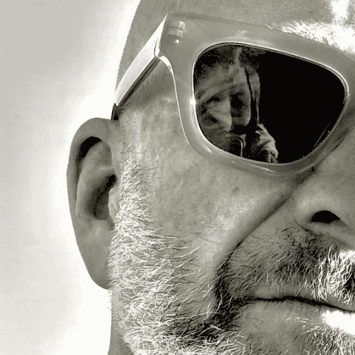 Close-up of a person wearing sunglasses with a reflection of another person inside the lens.