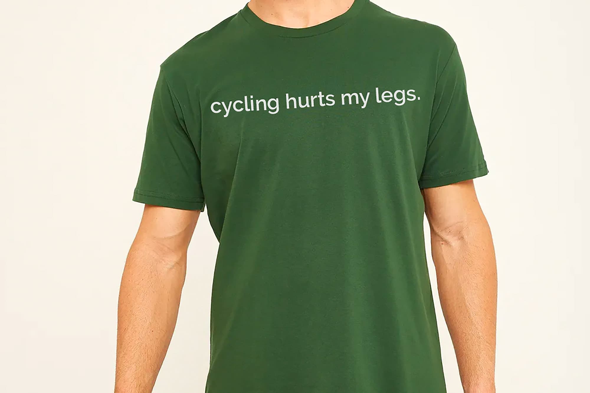 Green t-shirt with 'cycling hurts my legs' text on a plain background