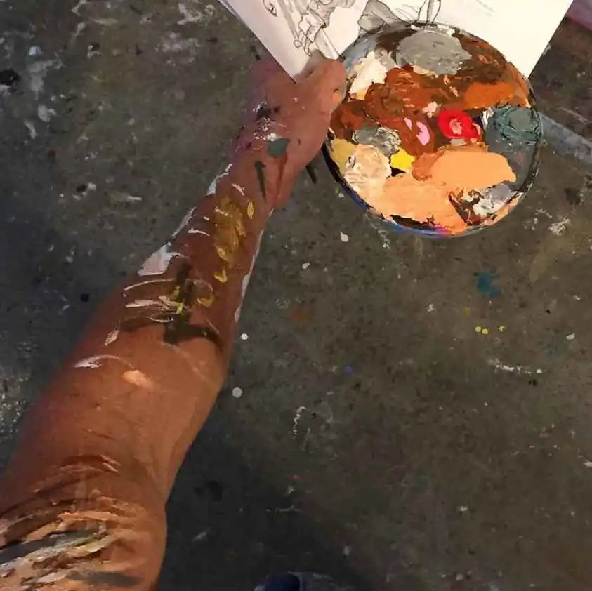 Artistic perspective of a hand holding a paintbrush over a palette with various colors on a textured surface.