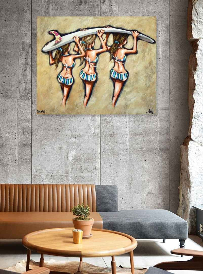 Painting of three women holding a surfboard on a wall above a living room setup with a couch and coffee table.