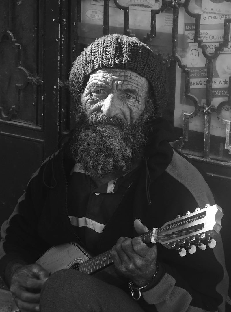 Man with a beard and knitted hat holding a guitar in a black and white photo.