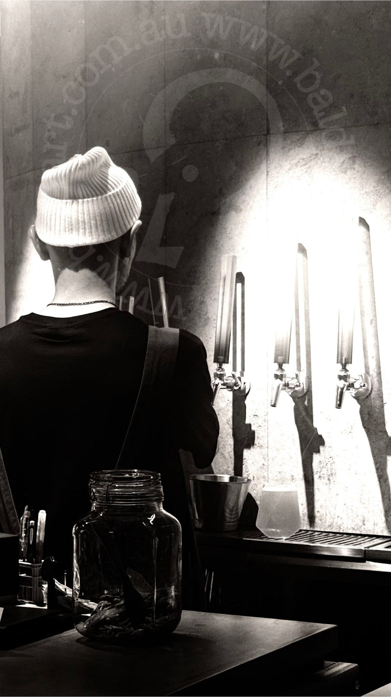 Person wearing a beanie standing in front of a bar with glasses and bottles.