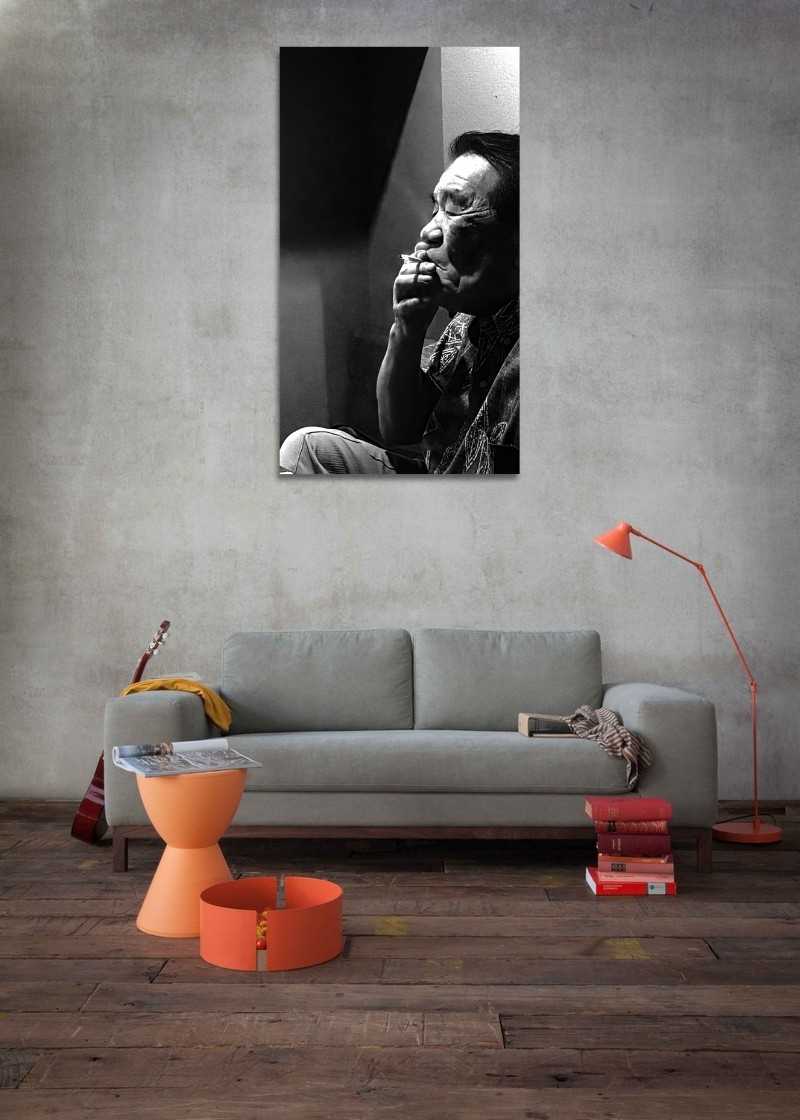 Living room with a gray sofa, orange coffee table, and lamp against a concrete wall with a large portrait.