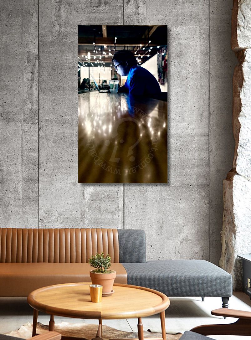 Framed photograph of a person sitting at a table in a restaurant, hanging on a concrete wall above a modern living room.