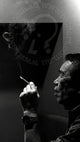 Black and white photo of a person smoking with a logo in the corner