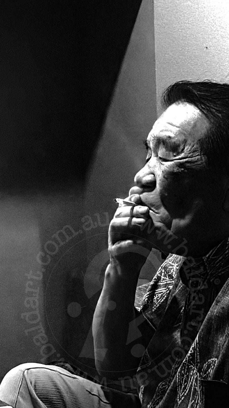 Black and white photo of a person with a patterned shirt sitting against a dark background.