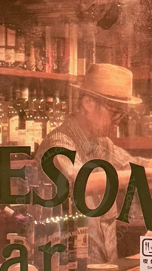 Person wearing a hat in a bar setting with shelves and bottles in the background