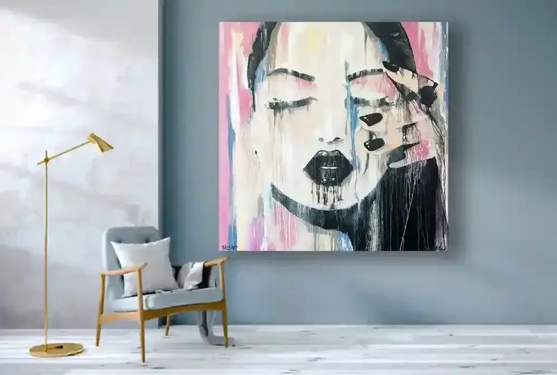 Abstract painting of a woman's face on a wall in a modern room with a chair and lamp.