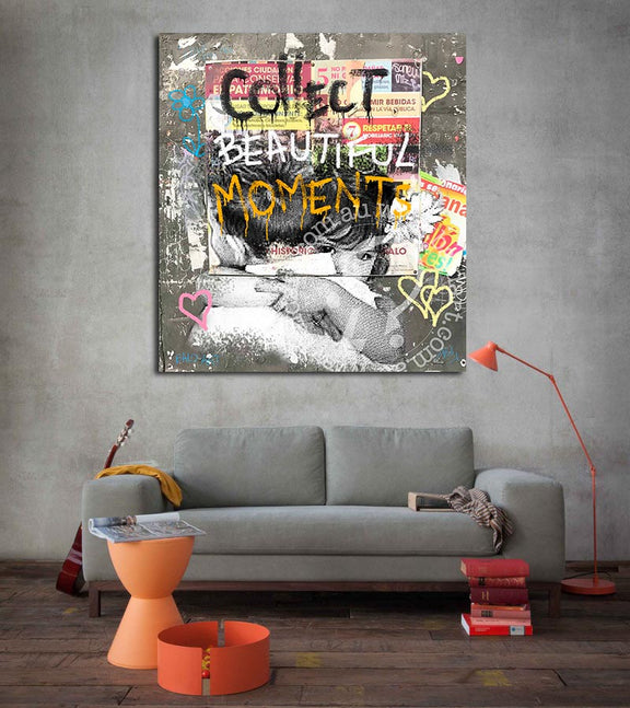 A canvas print featuring the text 'Collect Beautiful Moments' with a graffiti-style illustration, displayed on a wall above a gray sofa.