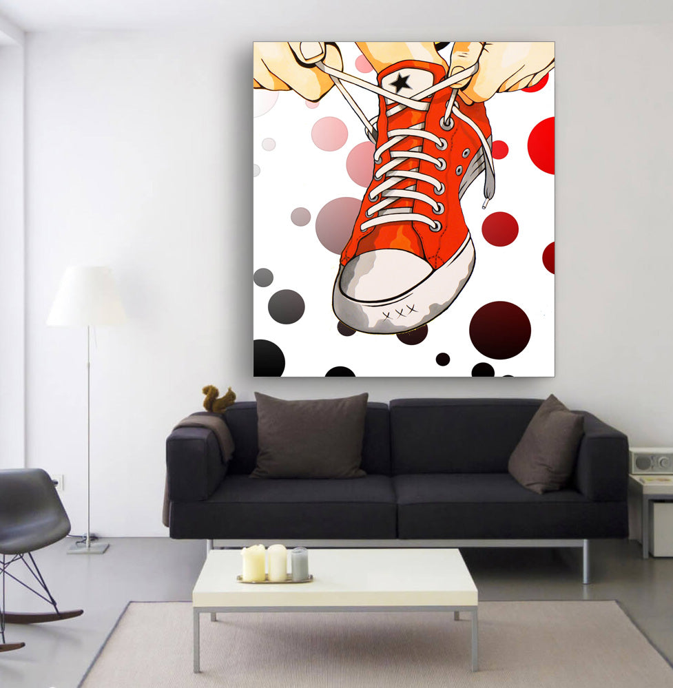 A canvas artwork featuring a red shoe with laces and dots around it, displayed on a wall in a living room setting.