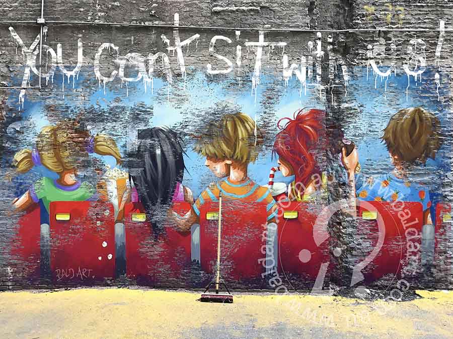 A vibrant mural showing children seated on a bench, engaged in conversation and laughter in a lively outdoor setting.